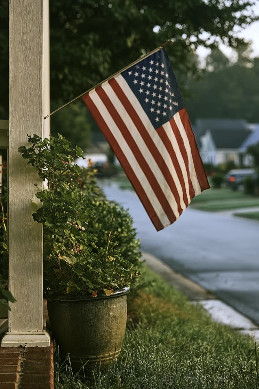 American flag hanging on a white column next to a potted plant outside a residential home