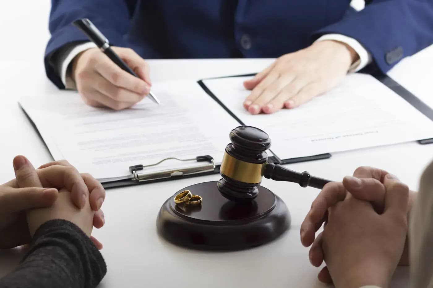 Judge's gavel and wedding rings on desk as lawyer signs divorce documents