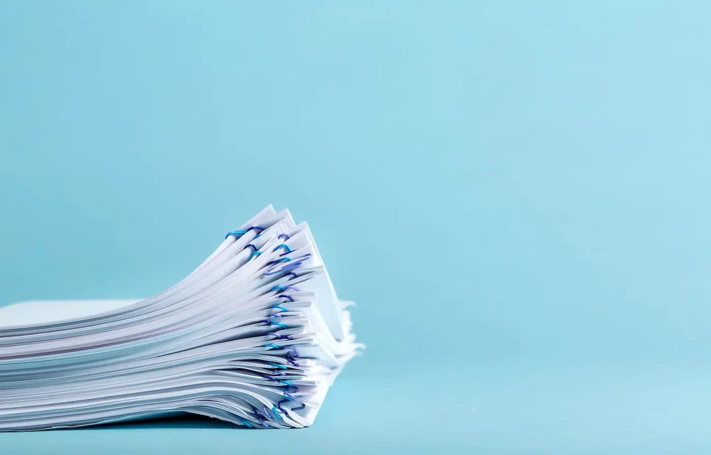 Stack of official documents with blue binding clips against light blue background
