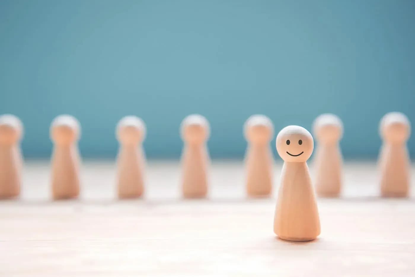 Figura de madera con rostro sonriente que sobresale entre figuras sencillas desenfocadas sobre un fondo azul