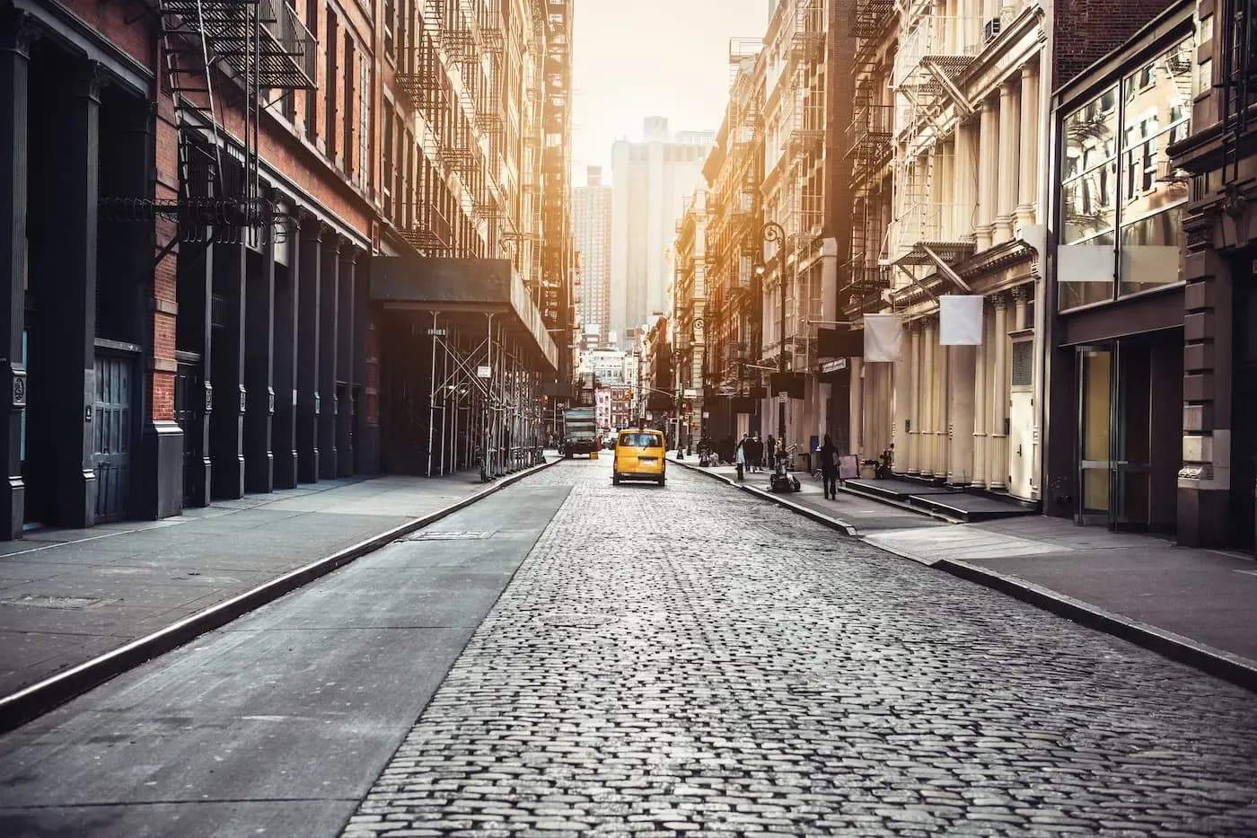 Sunny cobblestone street in New York City with yellow taxi cab, lined with historic buildings