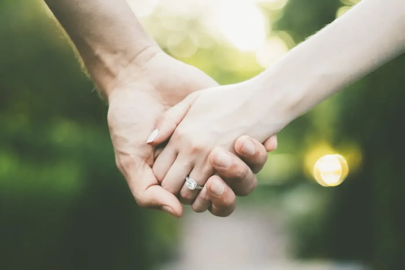 Close-up of a couple holding hands outdoors, woman wearing a diamond engagement ring