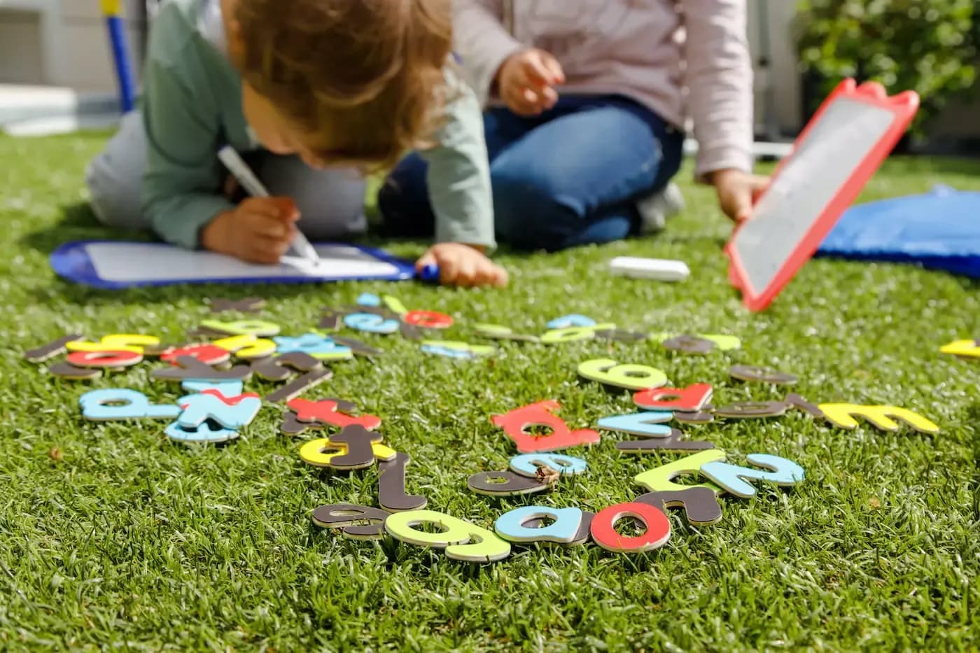 Young child and adult engaged in educational play with colorful number shapes on grass