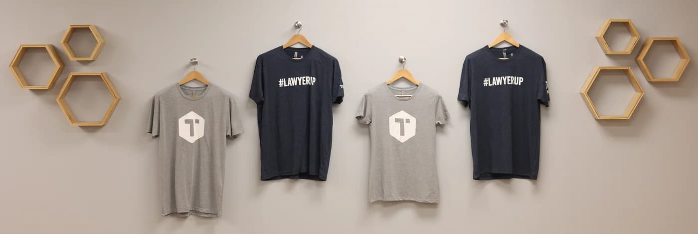 Four branded T-shirts on hangers, two gray with the Tingen logo and two navy with #LAWYERUP