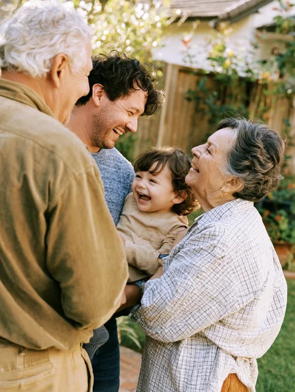 Grandparents, parent, and young child laughing together in a sunny backyard