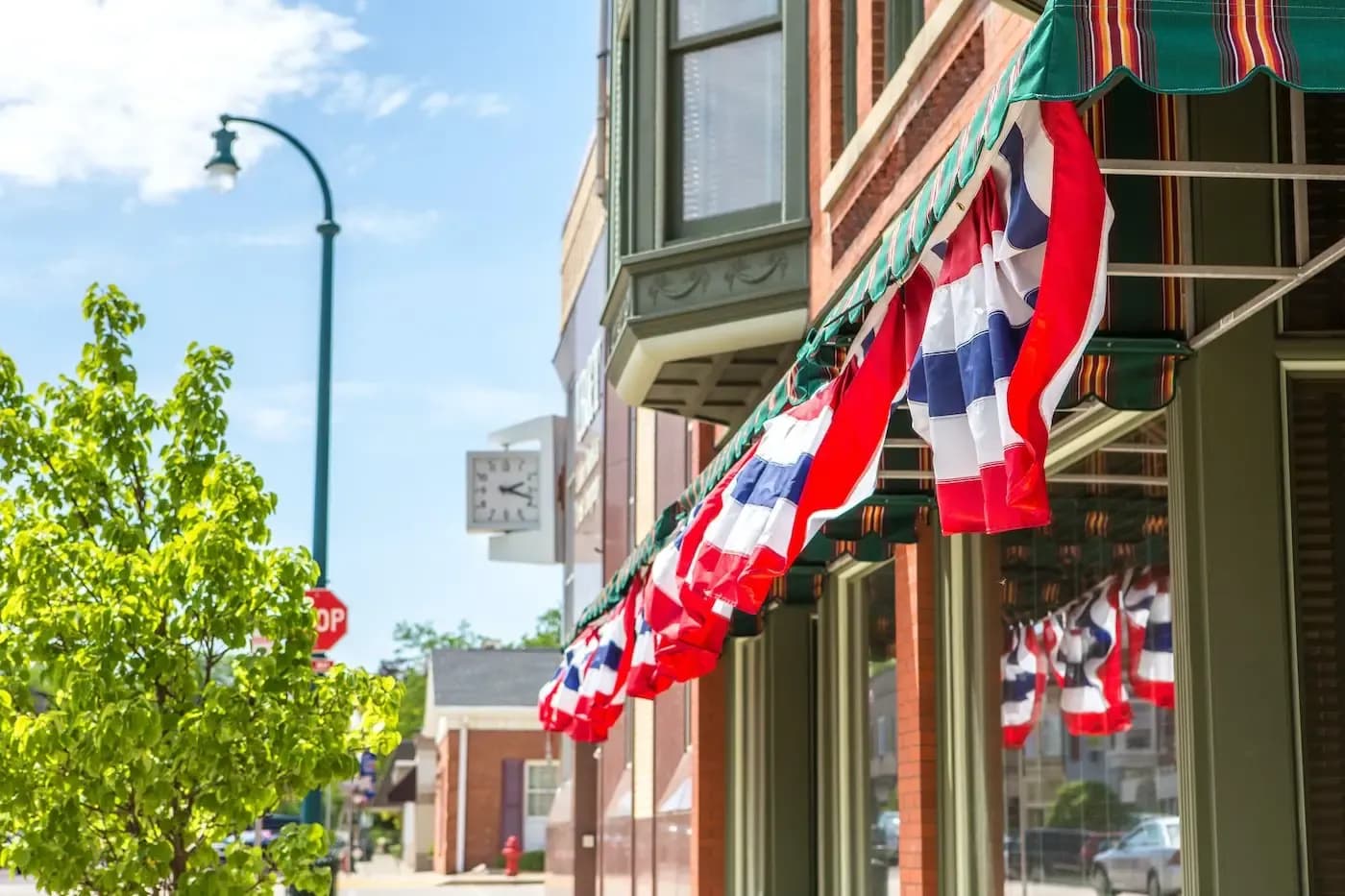 Red, white and blue decorative flags hanging from a storefront awning on a sunny downtown street