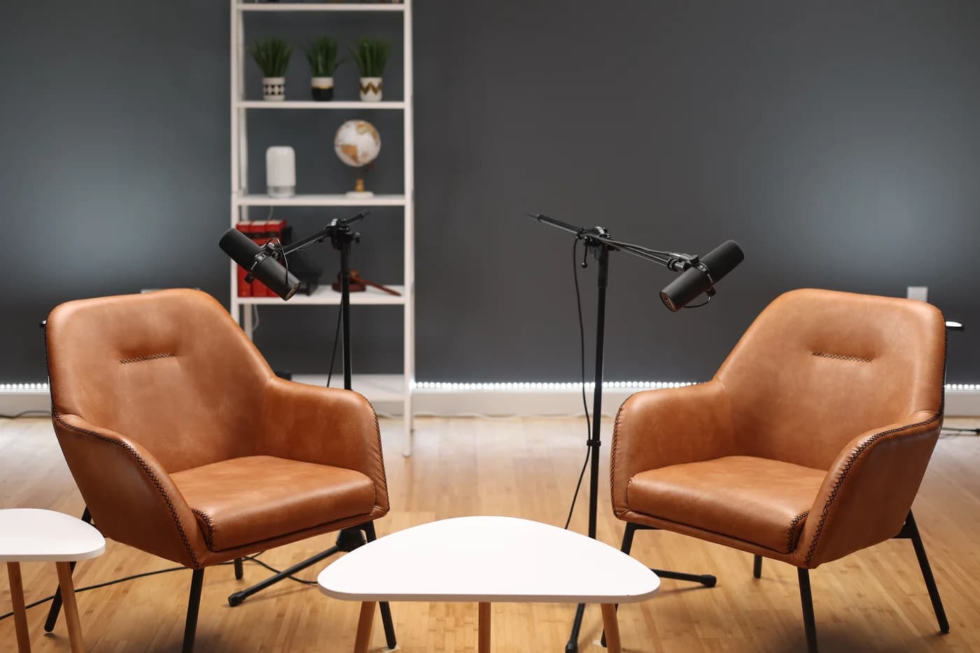 Two tan armchairs facing each other with boom microphones, set up for a podcast interview